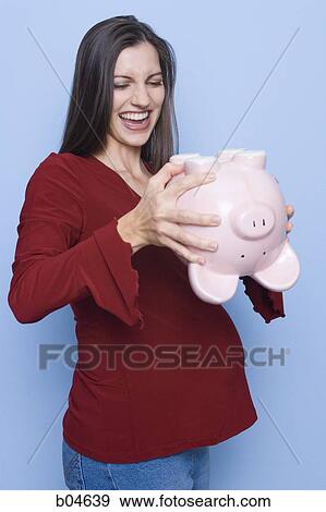 Stock Photo - Pregnant woman shaking piggy bank. Fotosearch