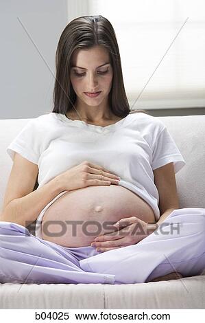 Pregnant woman sitting on sofa looking at belly View Large Photo Image Stock Photography - Pregnant woman sitting on sofa looking at belly. Fotosearch