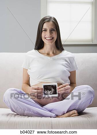 Pregnant woman sitting on sofa with ultrasound photo View Large Photo Image Stock Photo - Pregnant woman sitting on sofa with ultrasound photo. Fotosearch