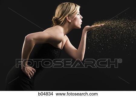 Picture - Profile of woman blowing gold dust from hand. Fotosearch