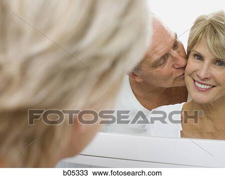 Stock Image - Reflection of mature couple kissing in mirror. Fotosearch