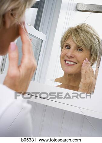 Stock Image - Reflection of mature woman in bathroom mirror. Fotosearch