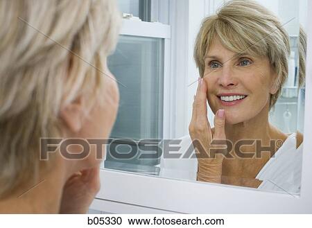 Stock Image - Reflection of mature woman smiling in bathroom mirror. Fotosearch
