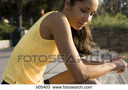 Stock Image - Side profile of woman sitting outdoors with bottled water. Fotosearch