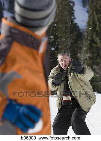 Stock Image - Son throwing a snowball at his father. Fotosearch