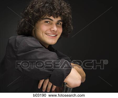 Stock Image - Teenage boy on chair smiling with arms crossed. Fotosearch