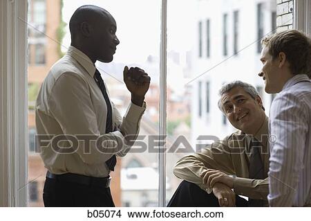 Picture - Three businessmen talking by large window. Fotosearch