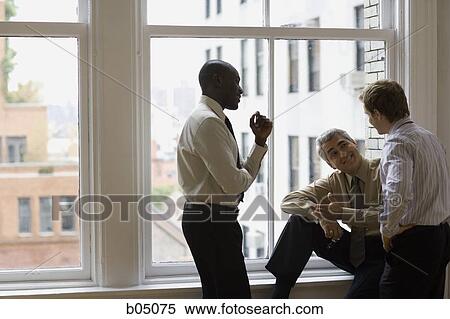 Stock Photography - Three businessmen talking by large window. Fotosearch