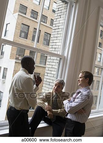Three businessmen talking in front of large window View Large Photo Image Stock Image - Three businessmen talking in front of large window. Fotosearch