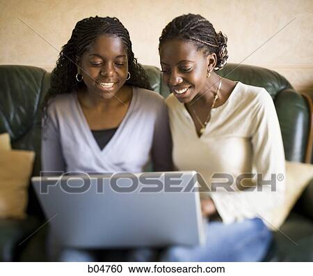 Two women sitting on sofa with laptop smiling View Large Photo Image Stock Image - Two women sitting on sofa with laptop smiling. Fotosearch