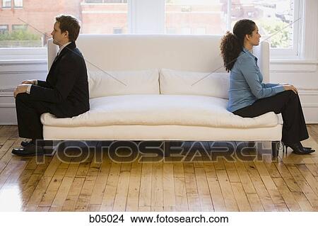 Picture - Woman and man sitting on sofa with backs to each other. Fotosearch
