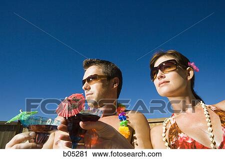 Stock Image - Woman and man with cocktails and sunglasses outdoors. Fotosearch