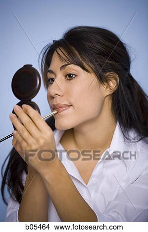 Picture - Woman applying lipstick with compact mirror. Fotosearch