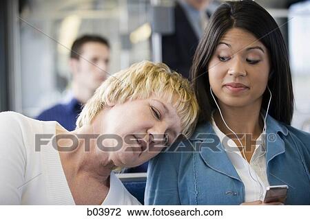 Stock Image - Woman asleep on another woman's shoulder on city bus or subway. Fotosearch