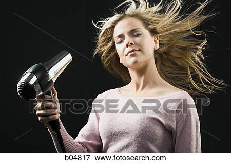 Stock Photo - Woman blow drying blonde hair with closed eyes. Fotosearch