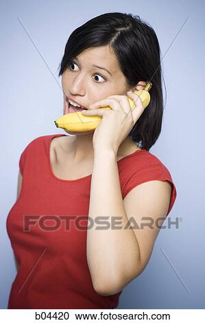 Stock Image - Woman holding a banana to her ear. Fotosearch