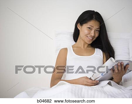 Stock Image - Woman in bed with magazine. Fotosearch