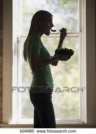Woman in front of window eating bowl of cereal View Large Photo Image Stock Image - Woman in front of window eating bowl of cereal. Fotosearch