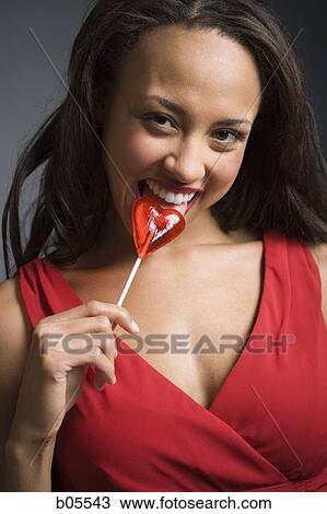 Stock Image - Woman licking heart shaped lollipop. Fotosearch