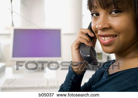 Stock Photo - Woman sitting at desk talking on telephone. Fotosearch