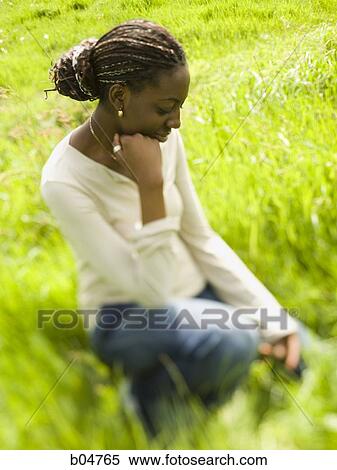 Stock Photography - Woman sitting in grass field. Fotosearch