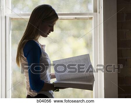 Stock Photograph - Woman standing at window reading. Fotosearch