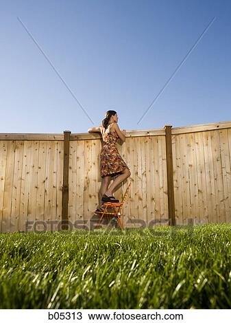 Woman standing on chair peeping over fence View Large Photo Image Stock Image - Woman standing on chair peeping over fence. Fotosearch