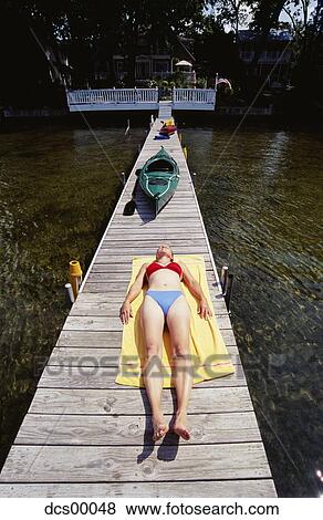 Stock Photo - Woman sunbathing on dock. Fotosearch