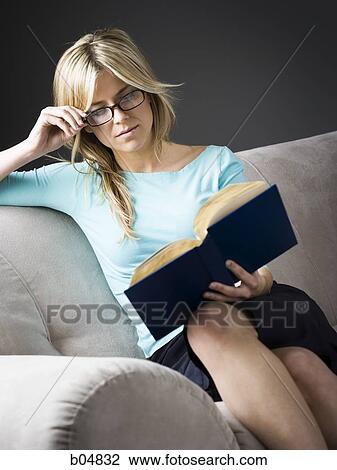Woman with glasses sitting on sofa reading View Large Photo Image Stock Image - Woman with glasses sitting on sofa reading. Fotosearch