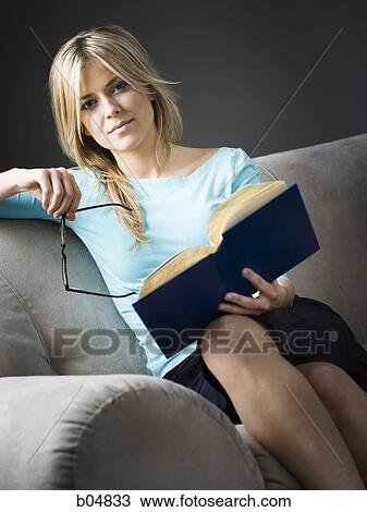 Woman with glasses sitting on sofa with book View Large Photo Image Stock Image - Woman with glasses sitting on sofa with book. Fotosearch
