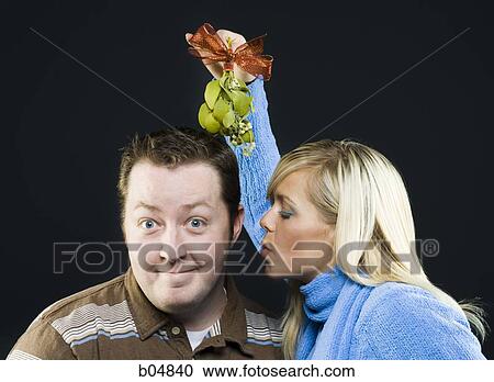 Stock Image - Woman with mistletoe giving man kiss. Fotosearch
