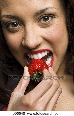 Stock Image - Woman with red lipstick eating strawberry. Fotosearch