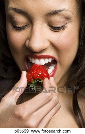 Stock Photo - Woman with red lipstick eating strawberry. Fotosearch