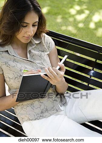 Woman writing in a notebook on a bench View Large Photo Image Stock Photo - Woman writing in a notebook on a bench. Fotosearch