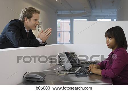 Stock Image - Young Businessman begging woman in office cubicle. Fotosearch