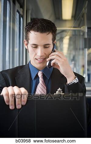 Stock Photo - Young businessman on cell phone on city bus or subway. Fotosearch