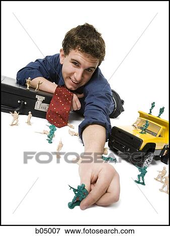 Young businessman playing with plastic army men and truck View Large Photo Image Stock Photo - Young businessman playing with plastic army men and truck. Fotosearch