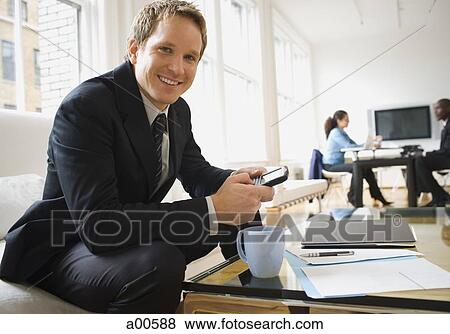 Young businessman sitting on sofa with blackberry smiling View Large Photo Image Stock Photo - Young businessman sitting on sofa with blackberry smiling. Fotosearch