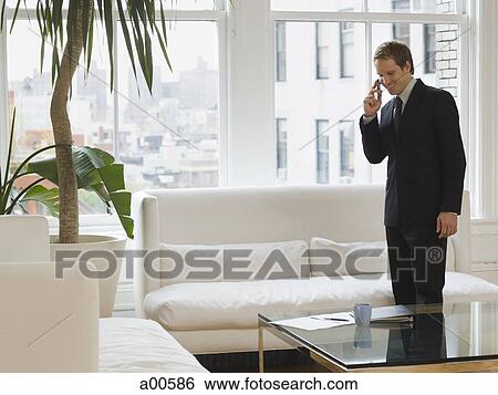 Young businessman talking on cellular phone in office with large windows View Large Photo Image Stock Photograph - Young businessman talking on cellular phone in office with large windows. Fotosearch