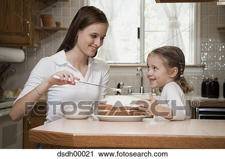 Young woman and child in a kitchen icing a cake View Large Photo Image Stock Image - Young woman and child in a kitchen icing a cake. Fotosearch