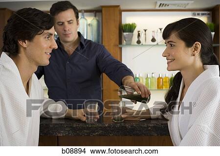 Bartender serving a young couple at a bar counter View Large Photo Image Picture - Bartender serving a young couple at a bar counter. Fotosearch