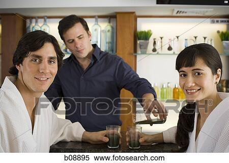 Bartender serving a young couple at a bar counter View Large Photo Image Stock Photography - Bartender serving a young couple at a bar counter. Fotosearch
