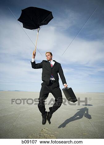 Stock Photo - Businessman jumping while holding an umbrella and a briefcase. Fotosearch