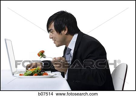Businessman simultaneously eating a salad and working on laptop View Large Photo Image Picture - Businessman simultaneously eating a salad and working on laptop. Fotosearch