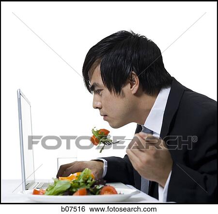 Businessman simultaneously eating a salad and working on laptop View Large Photo Image Stock Photograph - Businessman simultaneously eating a salad and working on laptop. Fotosearch