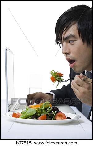 Businessman simultaneously eating a salad and working on laptop View Large Photo Image Stock Photography - Businessman simultaneously eating a salad and working on laptop. Fotosearch
