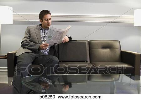 Businessman sitting on a couch and reading a newspaper View Large Photo Image Stock Image - Businessman sitting on a couch and reading a newspaper. Fotosearch