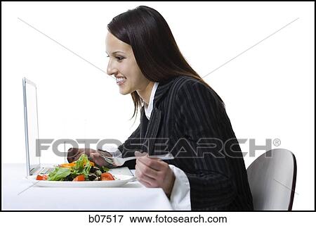 Businesswoman simultaneously eating a salad and working on laptop View Large Photo Image Stock Photo - Businesswoman simultaneously eating a salad and working on laptop. Fotosearch