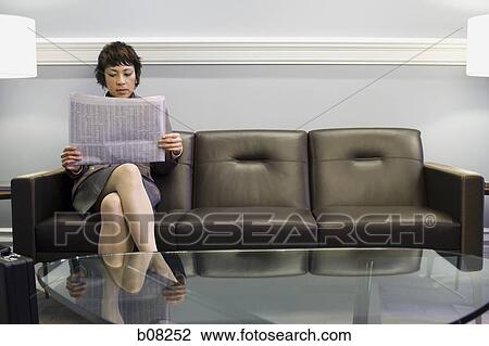 Businesswoman sitting on a couch and reading a newspaper View Large Photo Image Stock Image - Businesswoman sitting on a couch and reading a newspaper. Fotosearch