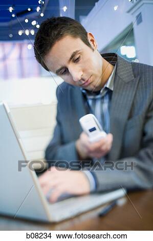 Close-up of a businessman using a cell phone in front of a laptop View Large Photo Image Picture - Close-up of a businessman using a cell phone in front of a laptop. Fotosearch